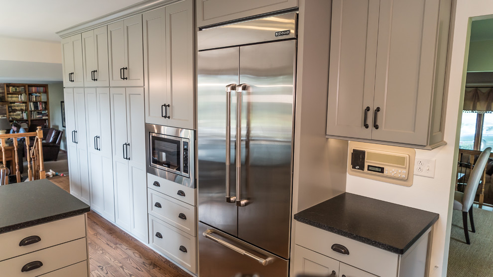Photo of a mid-sized country u-shaped eat-in kitchen in Chicago with a farmhouse sink, shaker cabinets, grey cabinets, granite benchtops, white splashback, subway tile splashback, stainless steel appliances, medium hardwood floors, a peninsula and brown floor.