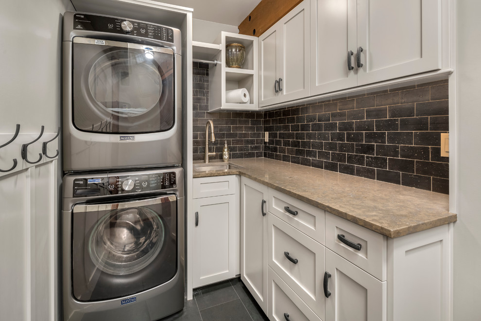 This is an example of a small country l-shaped dedicated laundry room in Seattle with an undermount sink, recessed-panel cabinets, white cabinets, limestone benchtops, beige walls, slate floors and a stacked washer and dryer.