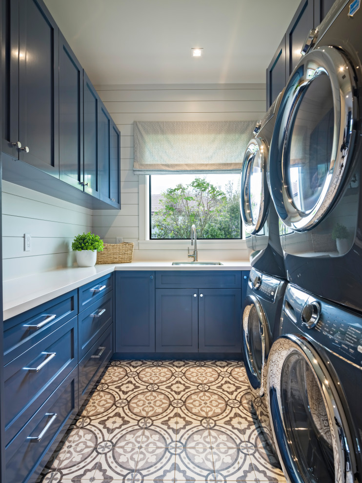 Photo of a medium sized modern u-shaped separated utility room in Miami with a submerged sink, shaker cabinets, blue cabinets, composite countertops, white walls, ceramic flooring, a stacked washer and dryer, multi-coloured floors, white worktops, tongue and groove walls and wood splashback.