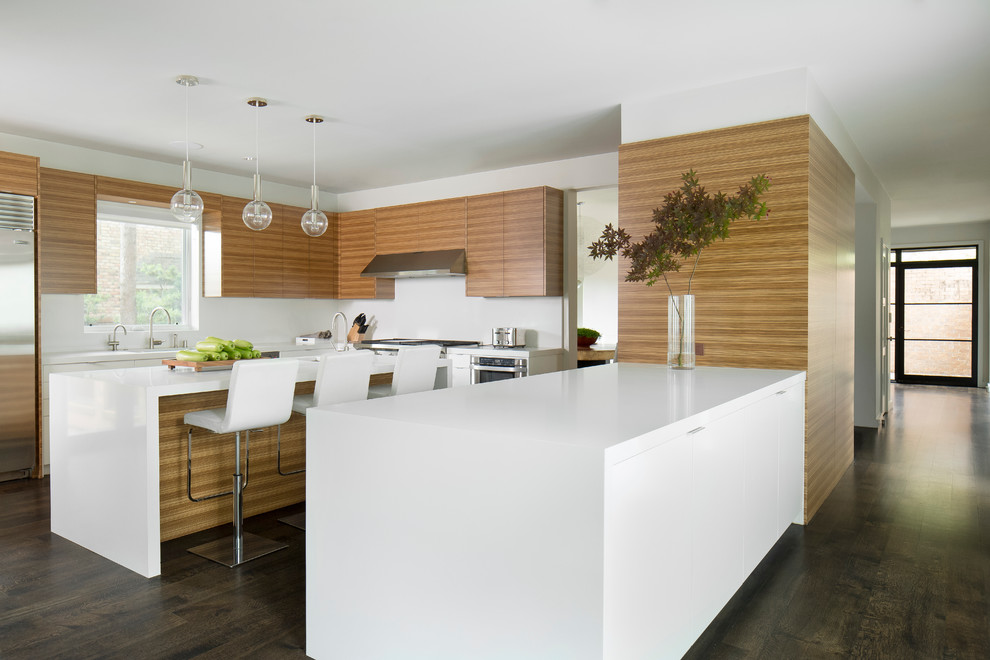 This is an example of a mid-sized contemporary u-shaped eat-in kitchen in Dallas with flat-panel cabinets, medium wood cabinets, solid surface benchtops, white splashback, stainless steel appliances, dark hardwood floors and with island.