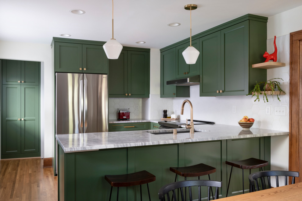 Foto på ett vintage grå kök, med en undermonterad diskho, gröna skåp, vitt stänkskydd, rostfria vitvaror, mellanmörkt trägolv, en halv köksö, brunt golv, granitbänkskiva och luckor med infälld panel