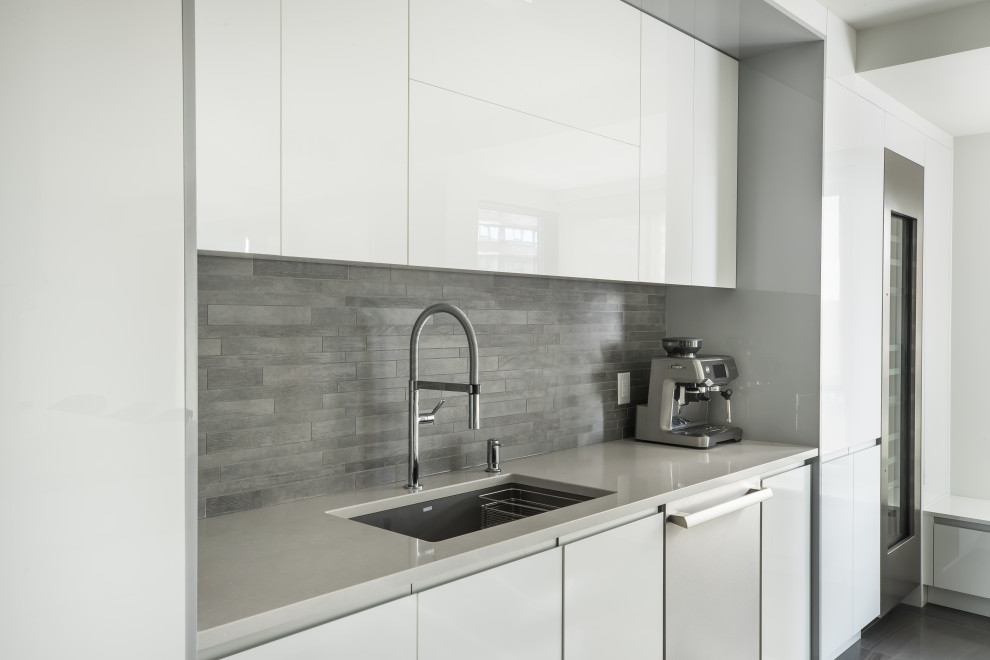 This is an example of an expansive modern galley separate kitchen in Montreal with a single-bowl sink, flat-panel cabinets, white cabinets, quartz benchtops, grey splashback, porcelain splashback, stainless steel appliances, porcelain floors, a peninsula, grey floor, grey benchtop and coffered.