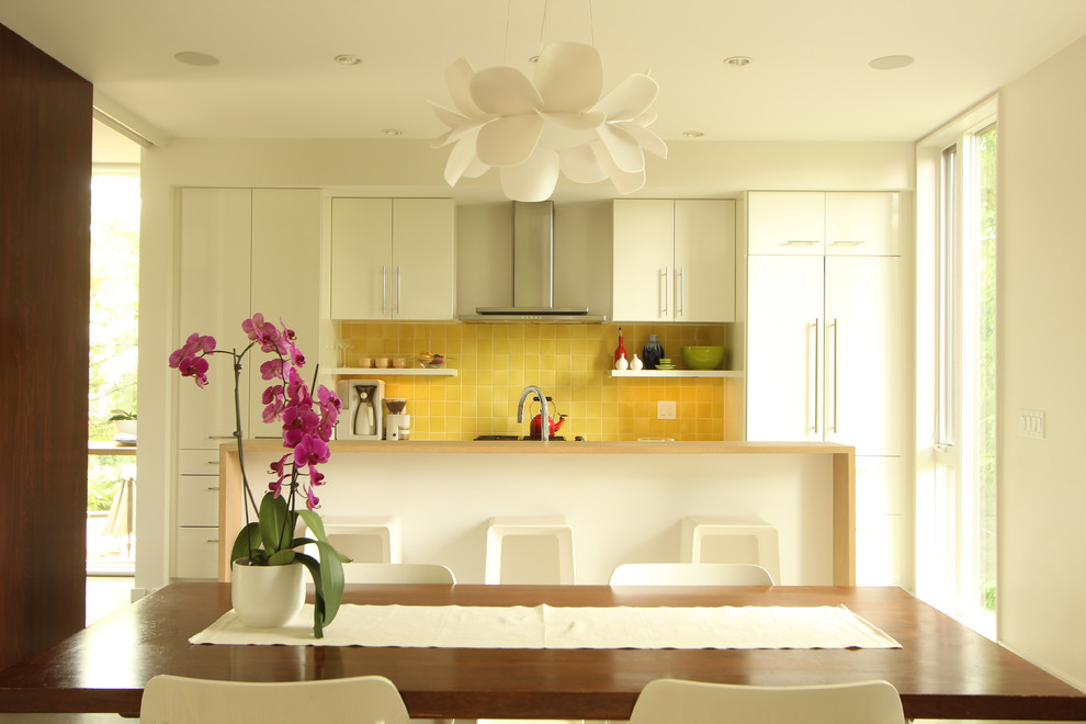 Photo of a small modern single-wall open plan kitchen in Other with a double-bowl sink, flat-panel cabinets, white cabinets, quartz benchtops, yellow splashback, ceramic splashback, panelled appliances, concrete floors and with island.