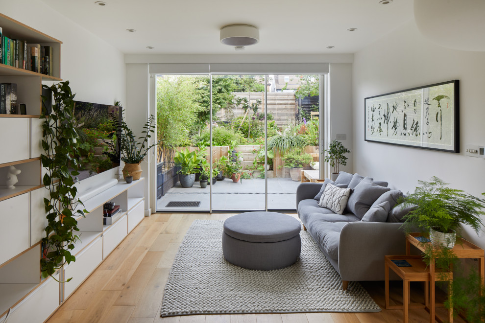 Idee per un soggiorno minimal di medie dimensioni e aperto con pareti bianche, parquet chiaro, TV a parete e pavimento marrone
