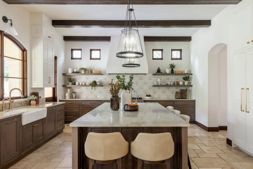 Eat-in kitchen - large mediterranean u-shaped travertine floor, beige floor and exposed beam eat-in kitchen idea in Orange County with a farmhouse sink, shaker cabinets, white cabinets, quartzite countertops, beige backsplash, mosaic tile backsplash, stainless steel appliances, an island and beige countertops