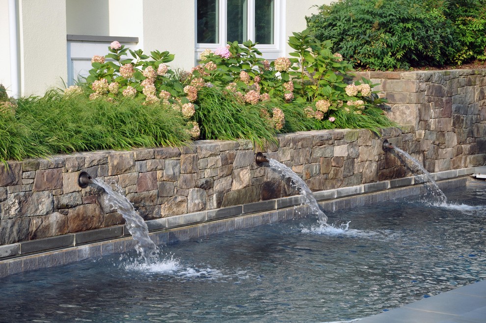 Inspiration for an expansive arts and crafts side yard rectangular lap pool in DC Metro with a water feature and natural stone pavers.