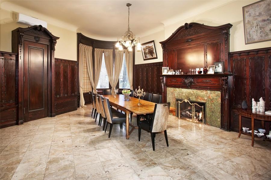 Photo of a dining room in New York with beige walls, marble floors, a standard fireplace and a wood fireplace surround.
