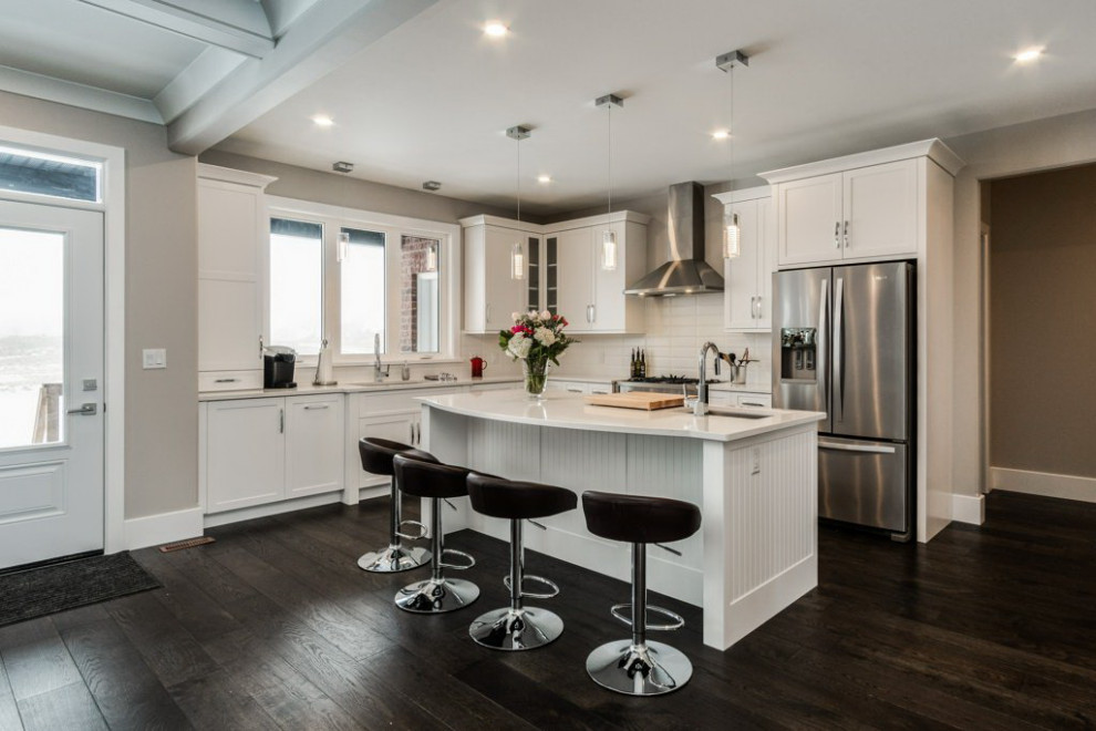 Open concept kitchen - mid-sized transitional l-shaped dark wood floor and brown floor open concept kitchen idea in Ottawa with an undermount sink, shaker cabinets, white cabinets, quartz countertops, white backsplash, subway tile backsplash, stainless steel appliances, an island and white countertops