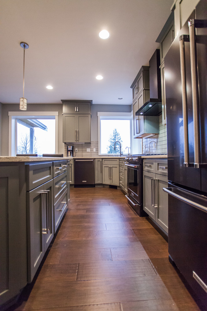 Photo of a large contemporary l-shaped open plan kitchen in Seattle with an undermount sink, shaker cabinets, grey cabinets, recycled glass benchtops, grey splashback, glass tile splashback, stainless steel appliances, with island, brown floor and dark hardwood floors.