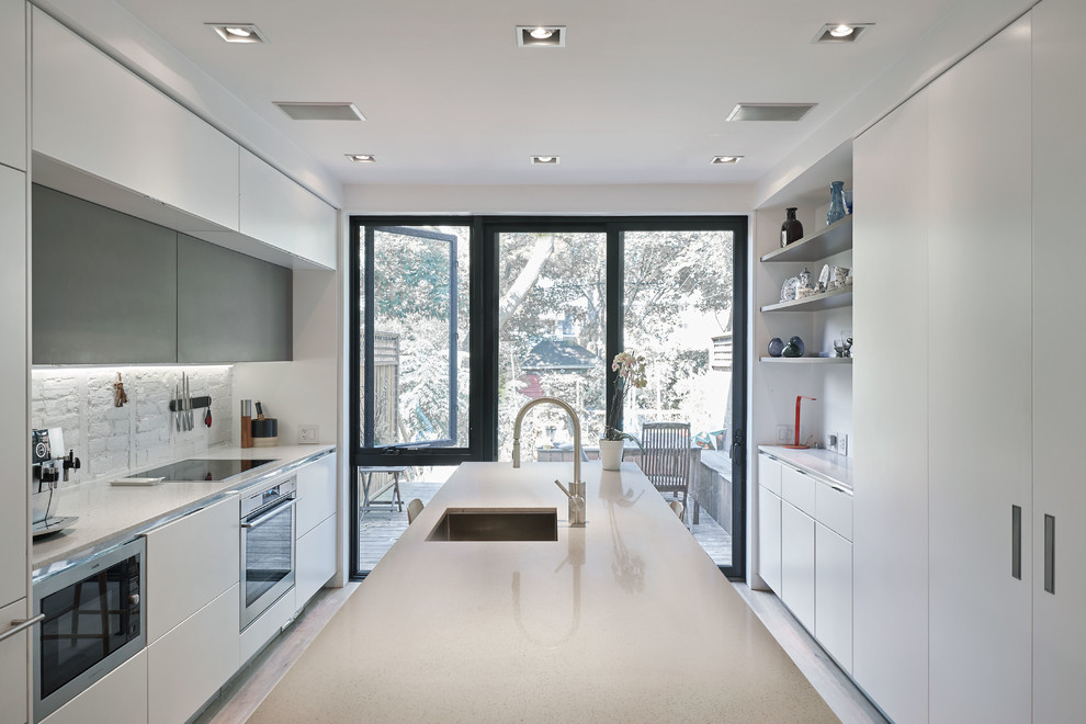 Inspiration for a mid-sized contemporary galley separate kitchen in Toronto with an undermount sink, flat-panel cabinets, white cabinets, copper benchtops, white splashback, brick splashback, panelled appliances, light hardwood floors and with island.