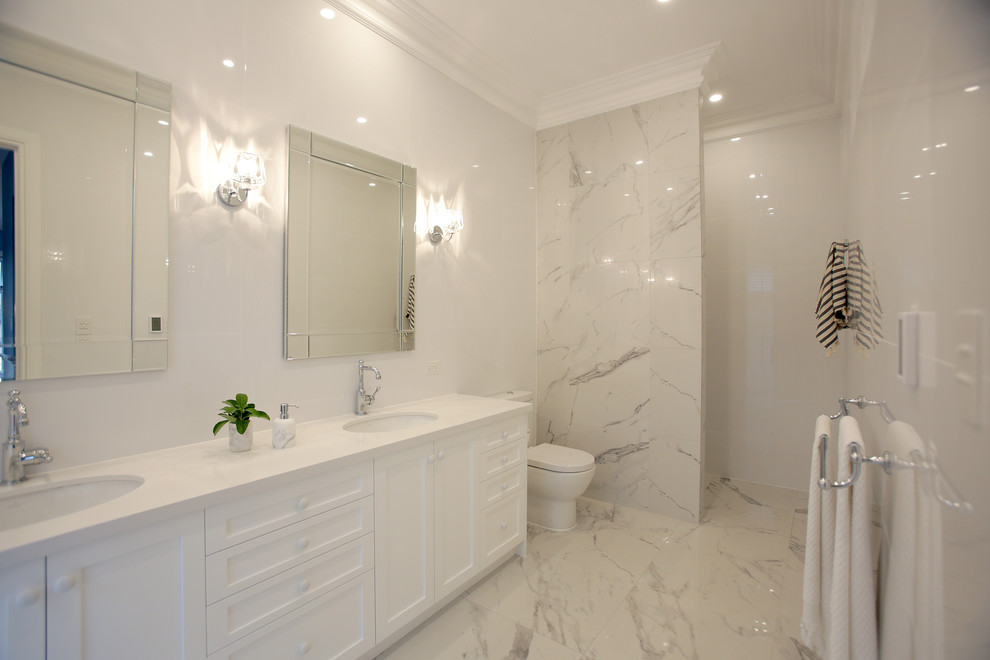 Design ideas for a large beach style master bathroom in Adelaide with shaker cabinets, white cabinets, a one-piece toilet, multi-coloured tile, stone tile, white walls, ceramic floors, an undermount sink, solid surface benchtops and a curbless shower.