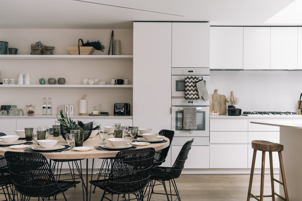 Contemporary galley eat-in kitchen in London with flat-panel cabinets, white cabinets, stainless steel appliances, light hardwood floors, with island, beige floor and white benchtop.