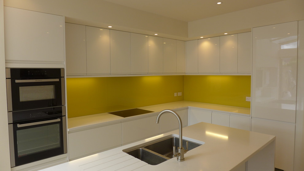 Inspiration for a mid-sized contemporary l-shaped open plan kitchen in Other with an undermount sink, flat-panel cabinets, white cabinets, quartzite benchtops, yellow splashback, glass sheet splashback, stainless steel appliances, porcelain floors, with island, beige floor and yellow benchtop.