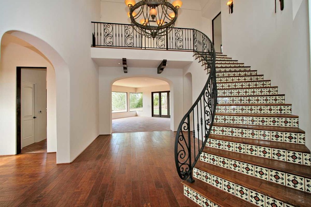 This is an example of a large mediterranean wood curved staircase in San Diego with tile risers and metal railing.