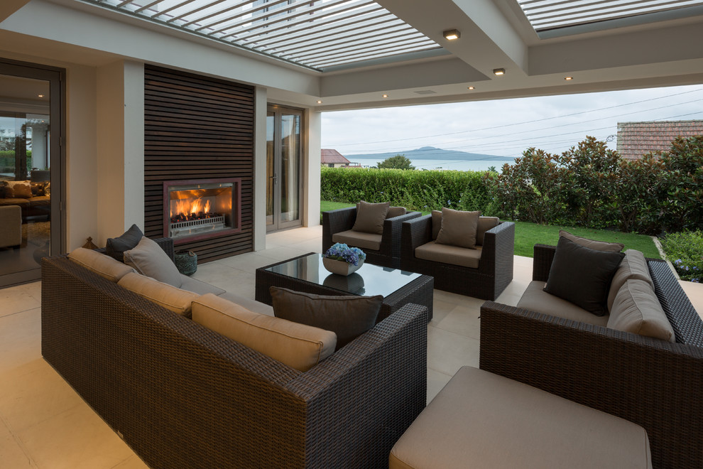 This is an example of a large contemporary backyard deck in Auckland with a fire feature and a roof extension.