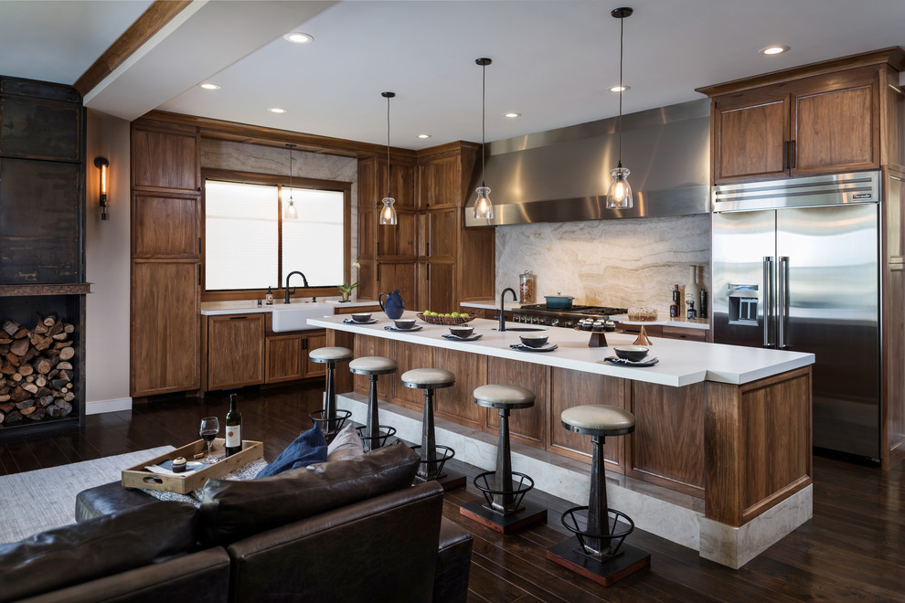Photo of a large transitional l-shaped open plan kitchen in San Diego with a farmhouse sink, recessed-panel cabinets, medium wood cabinets, quartz benchtops, beige splashback, marble splashback, stainless steel appliances, dark hardwood floors, with island and brown floor.