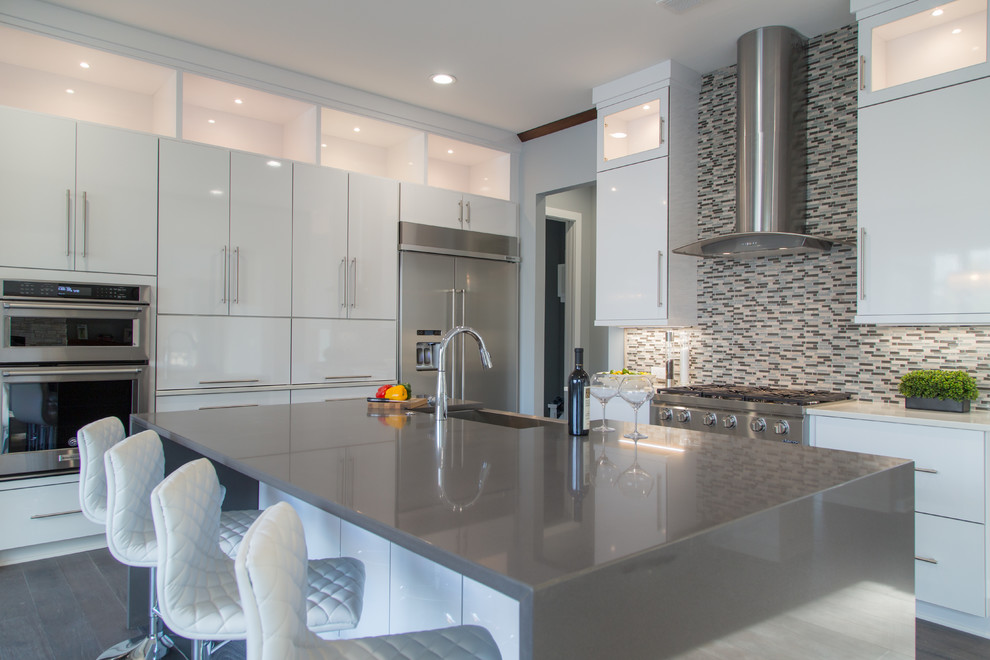 This is an example of a large contemporary l-shaped eat-in kitchen in Charlotte with a single-bowl sink, flat-panel cabinets, white cabinets, quartz benchtops, multi-coloured splashback, mosaic tile splashback, stainless steel appliances, dark hardwood floors and with island.