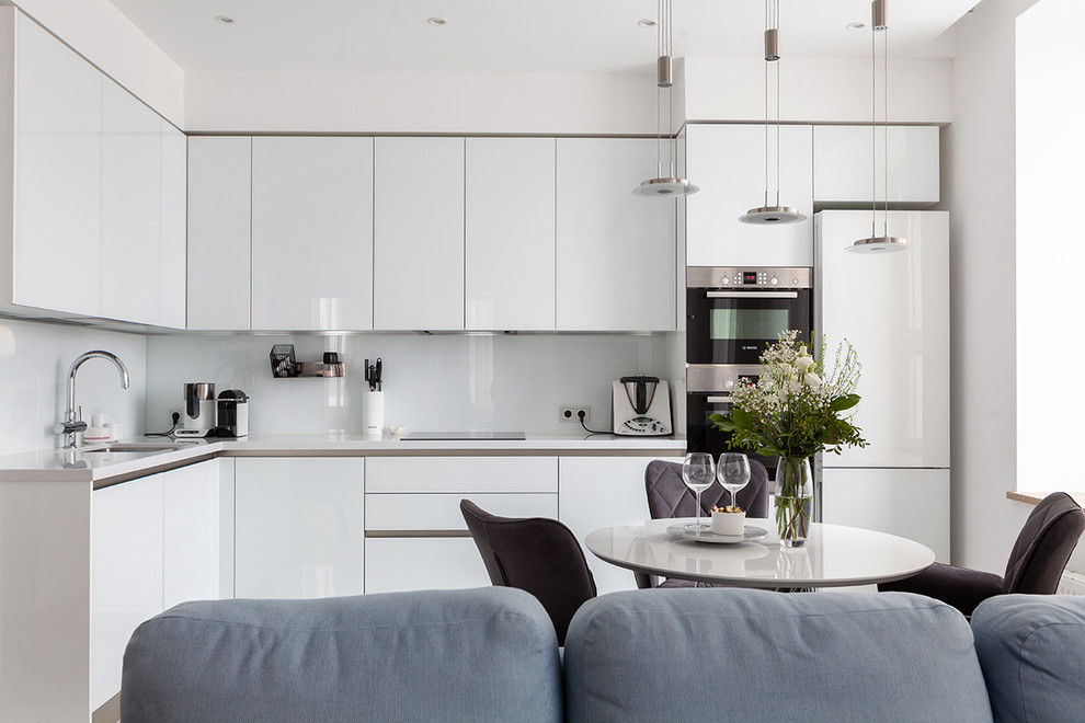 Inspiration for a contemporary l-shaped open plan kitchen in Moscow with an undermount sink, flat-panel cabinets, white cabinets, white splashback, stainless steel appliances, no island and white benchtop.