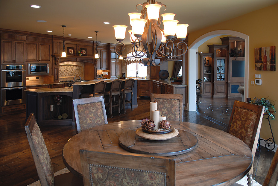 Photo of a large traditional l-shaped eat-in kitchen in Chicago with an undermount sink, raised-panel cabinets, dark wood cabinets, granite benchtops, multi-coloured splashback, ceramic splashback, stainless steel appliances, dark hardwood floors, with island, brown floor and multi-coloured benchtop.