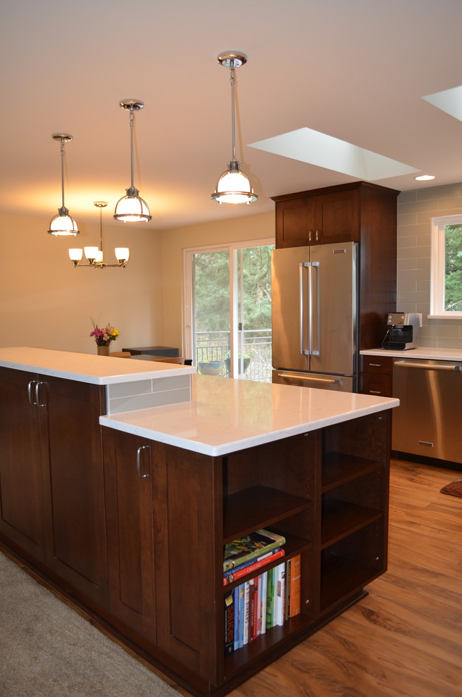 Inspiration for a mid-sized transitional l-shaped medium tone wood floor and brown floor open concept kitchen remodel in Seattle with an undermount sink, shaker cabinets, dark wood cabinets, quartz countertops, stainless steel appliances, an island, gray backsplash and subway tile backsplash