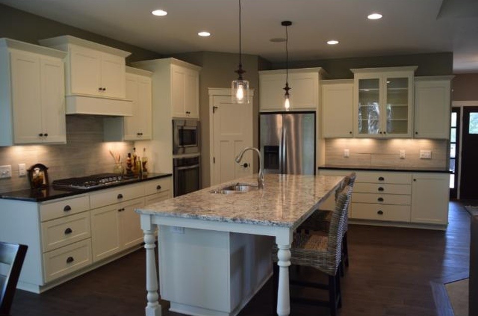 This is an example of a mid-sized transitional l-shaped open plan kitchen in Minneapolis with a double-bowl sink, shaker cabinets, white cabinets, granite benchtops, beige splashback, stone slab splashback, stainless steel appliances, dark hardwood floors and with island.