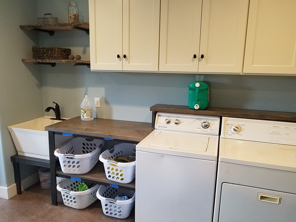 Large country l-shaped dedicated laundry room in Grand Rapids with an utility sink, shaker cabinets, white cabinets, wood benchtops, blue walls, concrete floors, a side-by-side washer and dryer, brown floor and brown benchtop.