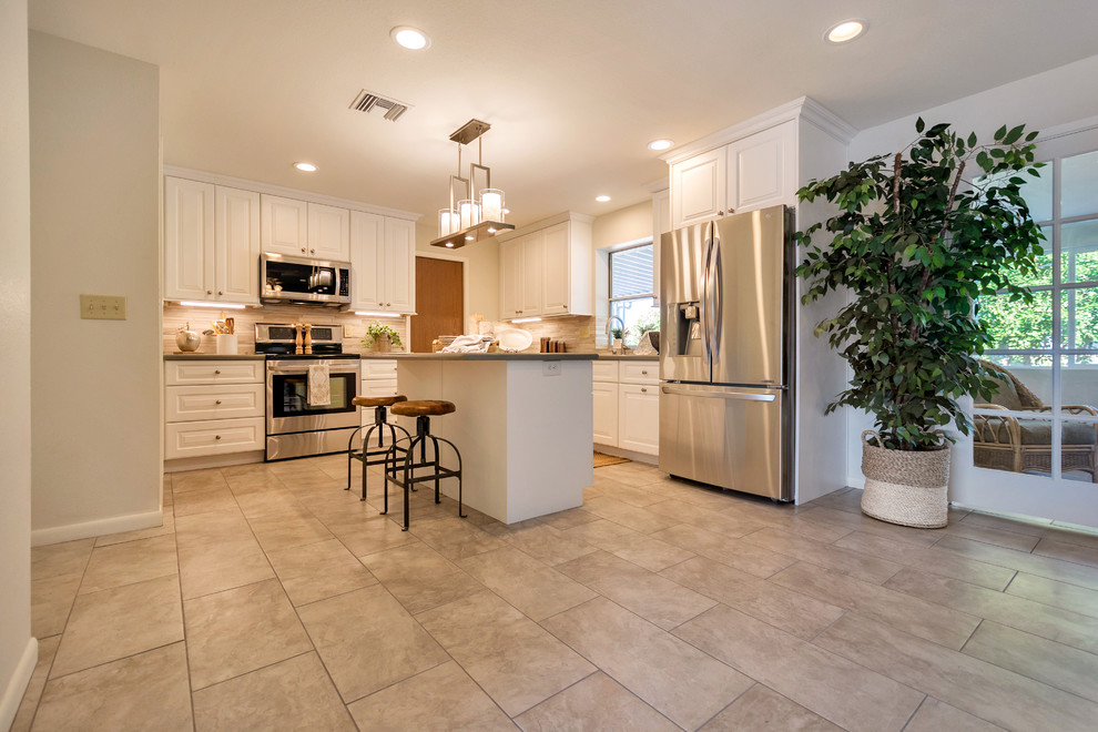 Example of a large transitional l-shaped porcelain tile open concept kitchen design in Phoenix with an undermount sink, raised-panel cabinets, white cabinets, quartz countertops, beige backsplash, porcelain backsplash, stainless steel appliances and an island
