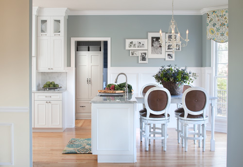 Bright eat-in kitchen with white shaker kitchen cabinet design, small island with marble countertop, blue walls, and round upholstered bar stools around a dining table.
