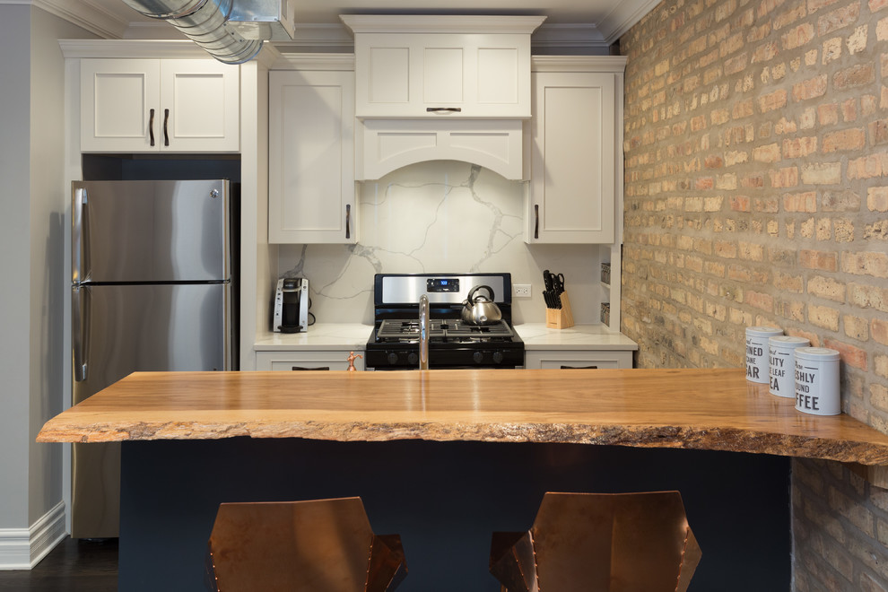 Mid-sized industrial galley open plan kitchen in Chicago with dark hardwood floors, brown floor, an undermount sink, flat-panel cabinets, white cabinets, wood benchtops, white splashback, marble splashback, stainless steel appliances and with island.