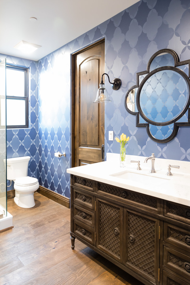 This is an example of a mediterranean 3/4 bathroom in Los Angeles with shaker cabinets, dark wood cabinets, a corner shower, a two-piece toilet, blue tile, blue walls, light hardwood floors and an undermount sink.