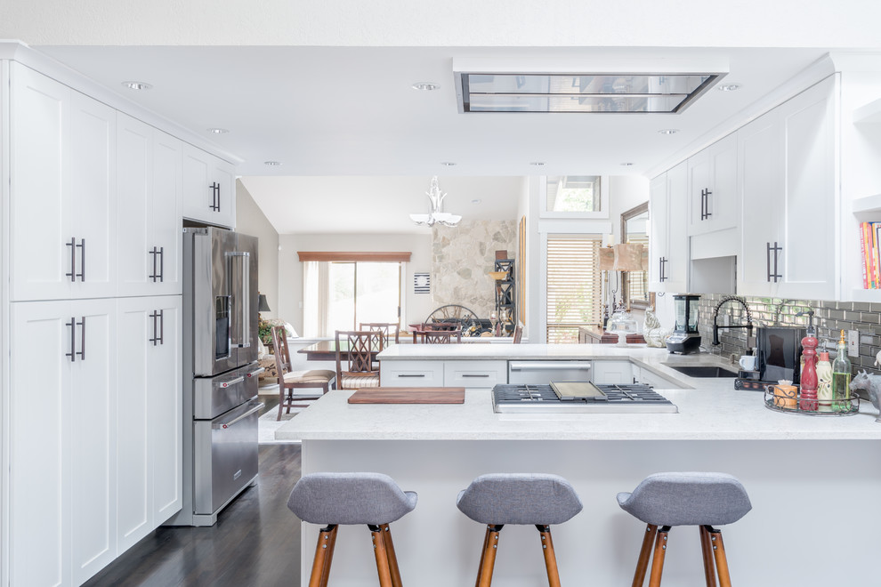 Inspiration for a mid-sized transitional u-shaped dark wood floor and brown floor eat-in kitchen remodel in Seattle with an undermount sink, white cabinets, metallic backsplash, stainless steel appliances, a peninsula, shaker cabinets, metal backsplash and white countertops