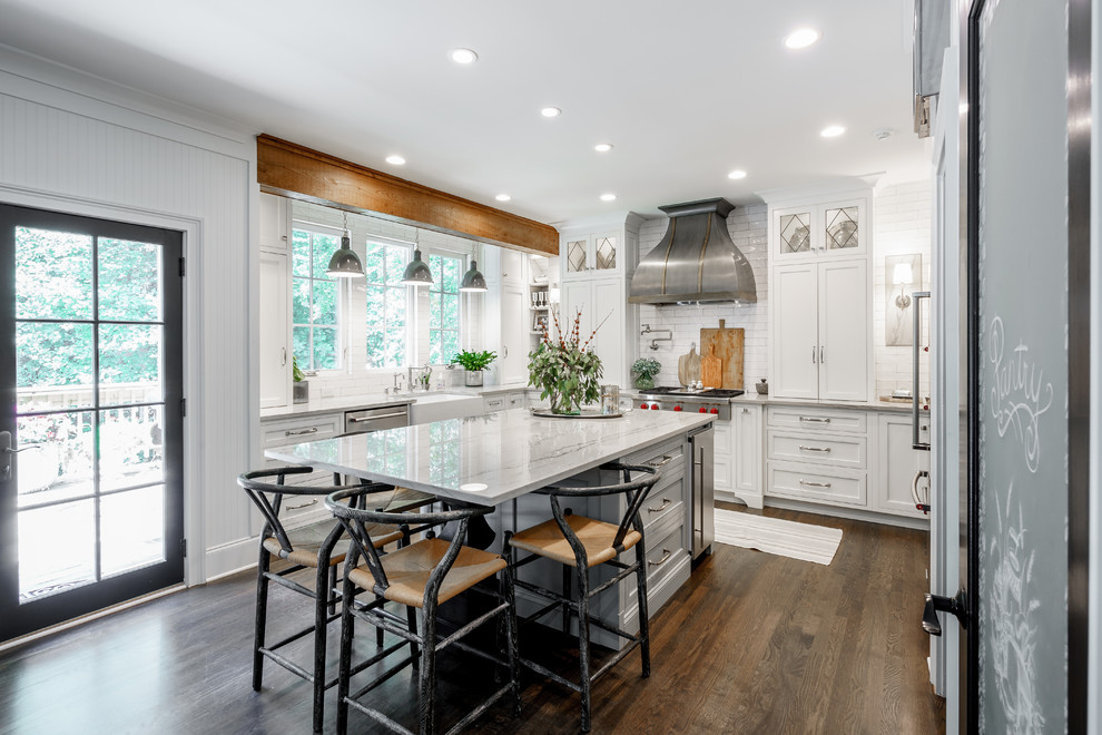 Mid-sized country u-shaped eat-in kitchen in Atlanta with white cabinets, quartzite benchtops, white splashback, with island, a farmhouse sink, shaker cabinets, subway tile splashback, stainless steel appliances, dark hardwood floors, brown floor and white benchtop.