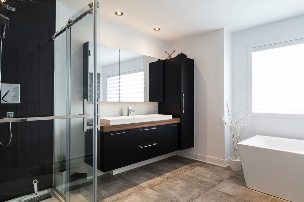 Mid-sized contemporary master wet room bathroom in Montreal with flat-panel cabinets, black cabinets, a japanese tub, black tile, ceramic tile, grey walls, a vessel sink, laminate benchtops, grey floor and a sliding shower screen.