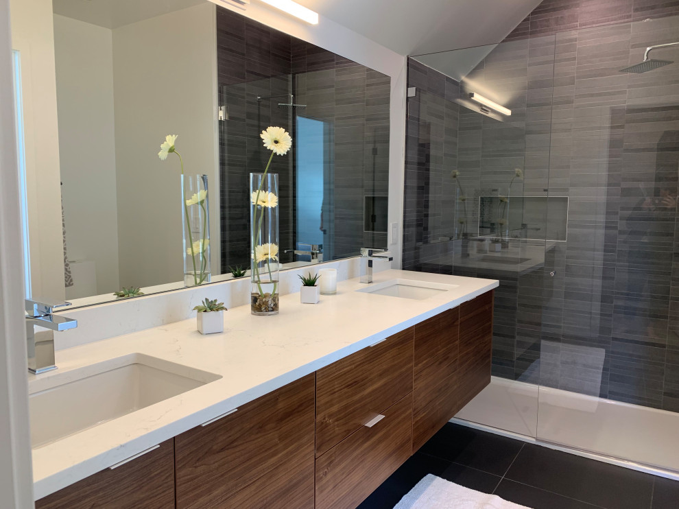 Photo of a large modern master bathroom in Albuquerque with medium wood cabinets, an alcove shower, gray tile, porcelain tile, white walls, porcelain floors, an undermount sink, engineered quartz benchtops, black floor, a sliding shower screen and white benchtops.