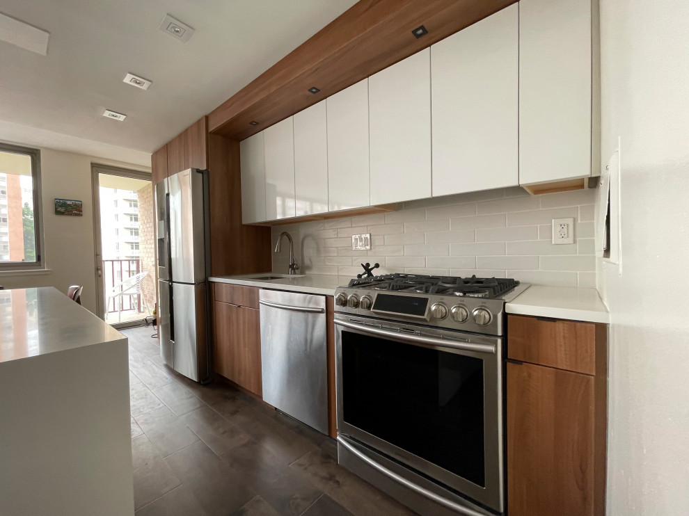 Small modern single-wall open plan kitchen in DC Metro with a drop-in sink, flat-panel cabinets, white cabinets, quartzite benchtops, white splashback, ceramic splashback, stainless steel appliances, medium hardwood floors, with island, brown floor and white benchtop.