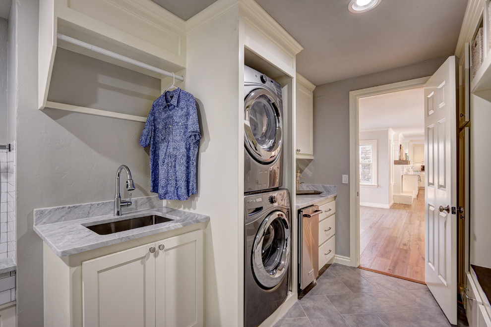 Large transitional galley utility room in Oklahoma City with an undermount sink, shaker cabinets, white cabinets, grey walls, ceramic floors, a stacked washer and dryer, marble benchtops, grey floor and grey benchtop.