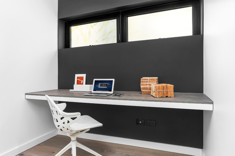 This is an example of a small contemporary study room in Sydney with multi-coloured walls, medium hardwood floors, a built-in desk and brown floor.