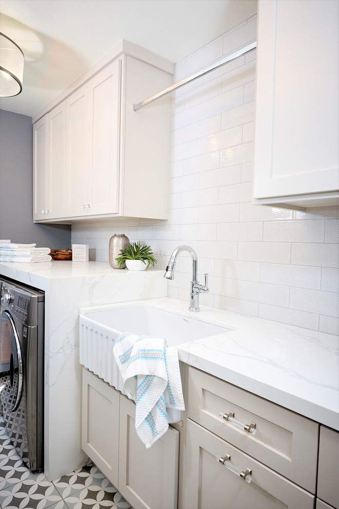 Photo of a small beach style single-wall utility room in San Diego with a farmhouse sink, recessed-panel cabinets, grey cabinets, quartz benchtops, white walls, ceramic floors, a side-by-side washer and dryer, grey floor and white benchtop.