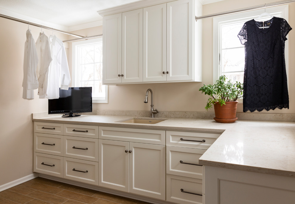 This is an example of a large transitional dedicated laundry room in Kansas City with an undermount sink, recessed-panel cabinets, white cabinets, quartzite benchtops, beige walls, porcelain floors, a side-by-side washer and dryer, brown floor and beige benchtop.