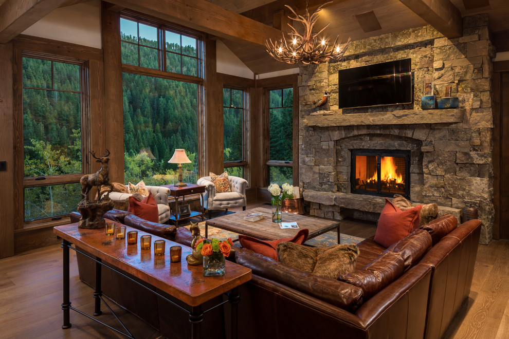 Mid-sized country open concept living room in Other with white walls, medium hardwood floors, a stone fireplace surround, a wall-mounted tv, brown floor and a standard fireplace.