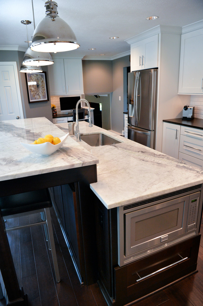 Inspiration for a transitional dark wood floor kitchen remodel in Cleveland with a drop-in sink, recessed-panel cabinets, white backsplash, ceramic backsplash, stainless steel appliances and an island