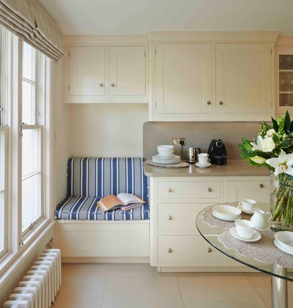 This is an example of a large traditional galley eat-in kitchen in London with white cabinets, shaker cabinets, quartz benchtops and limestone floors.