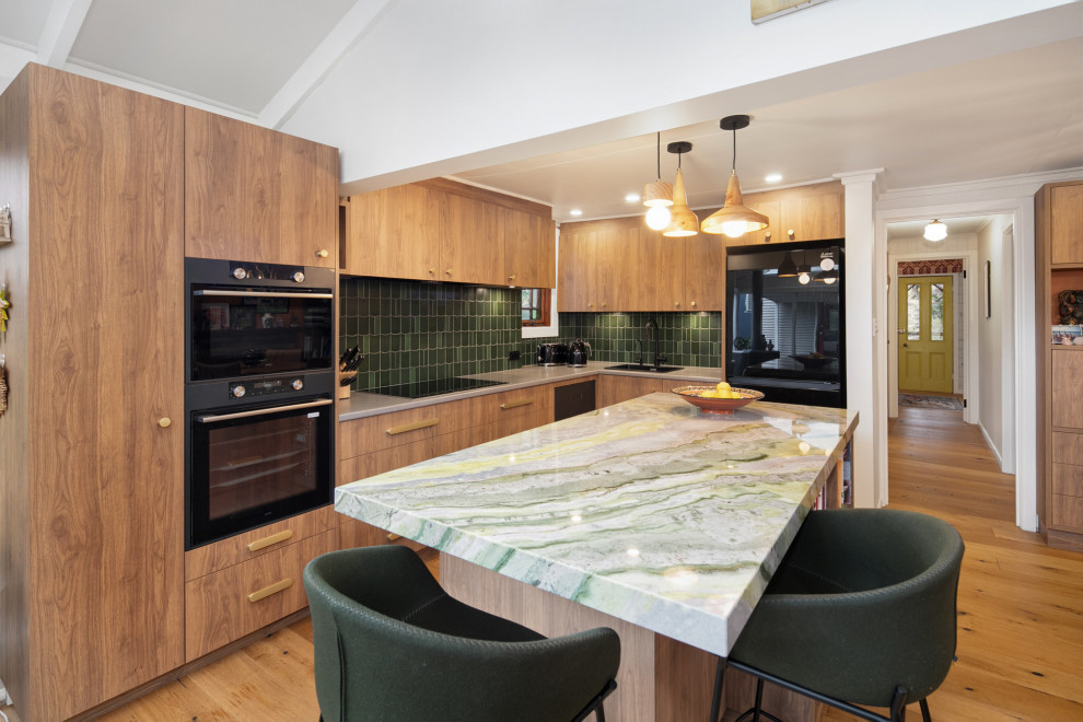 Inspiration for a mid-sized eclectic l-shaped open plan kitchen in Geelong with a drop-in sink, flat-panel cabinets, medium wood cabinets, green splashback, ceramic splashback, black appliances, medium hardwood floors, with island, green benchtop, vaulted and quartzite benchtops.