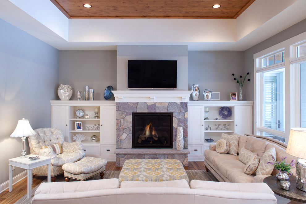 Photo of a mid-sized traditional open concept living room in Minneapolis with grey walls, medium hardwood floors, a standard fireplace, a stone fireplace surround and a wall-mounted tv.
