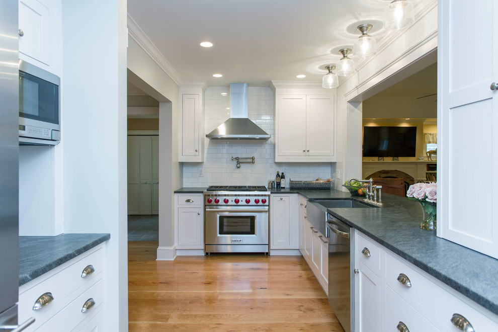 This is an example of a mid-sized transitional l-shaped eat-in kitchen in Boston with a farmhouse sink, white cabinets, granite benchtops, white splashback, stainless steel appliances, medium hardwood floors, no island, shaker cabinets and ceramic splashback.