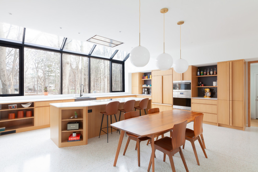 Photo of a midcentury l-shaped eat-in kitchen in Indianapolis with a farmhouse sink, flat-panel cabinets, medium wood cabinets, granite benchtops, panelled appliances, terrazzo floors, with island, white benchtop and white floor.
