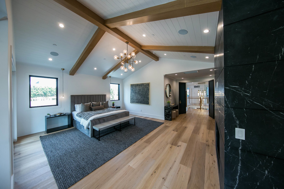 This is an example of a large modern master bedroom in Los Angeles with white walls, light hardwood floors, a standard fireplace, a tile fireplace surround, beige floor and wood.