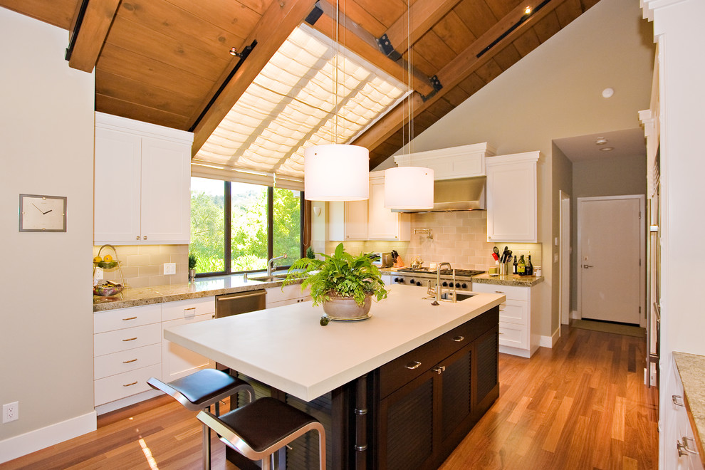 Inspiration for a large tropical u-shaped eat-in kitchen in San Francisco with a drop-in sink, dark wood cabinets, quartzite benchtops, grey splashback, stone tile splashback, stainless steel appliances and medium hardwood floors.