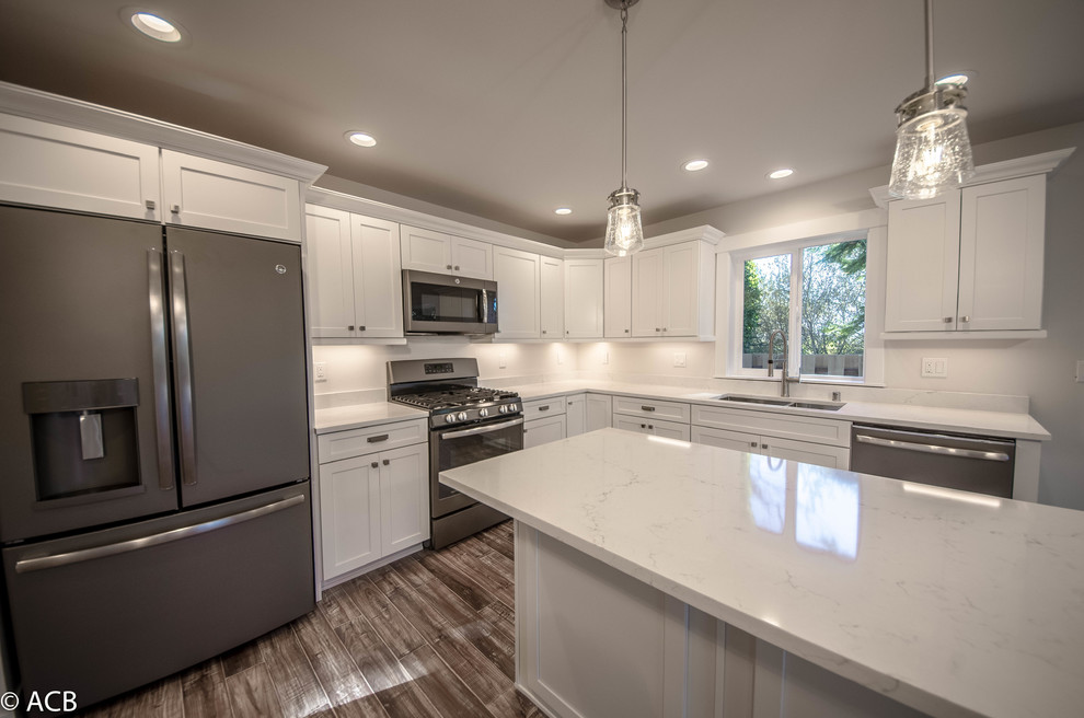 Beach style open plan kitchen in Seattle with a double-bowl sink, shaker cabinets, white cabinets, quartz benchtops, white splashback, coloured appliances, laminate floors, with island and brown floor.