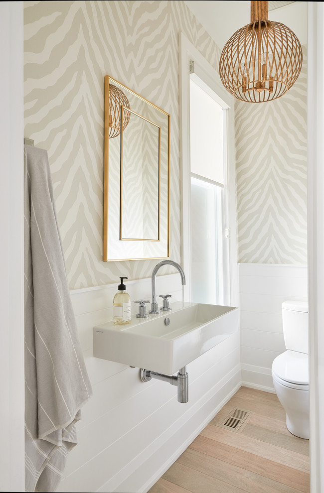 Inspiration for a transitional powder room in Toronto with beige walls, light hardwood floors, a wall-mount sink and beige floor.